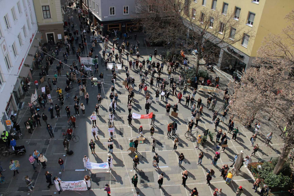 Menschen stehen mit Abstand gleichmäßig über einen Platz verteilt am Klimastreik in Graz
